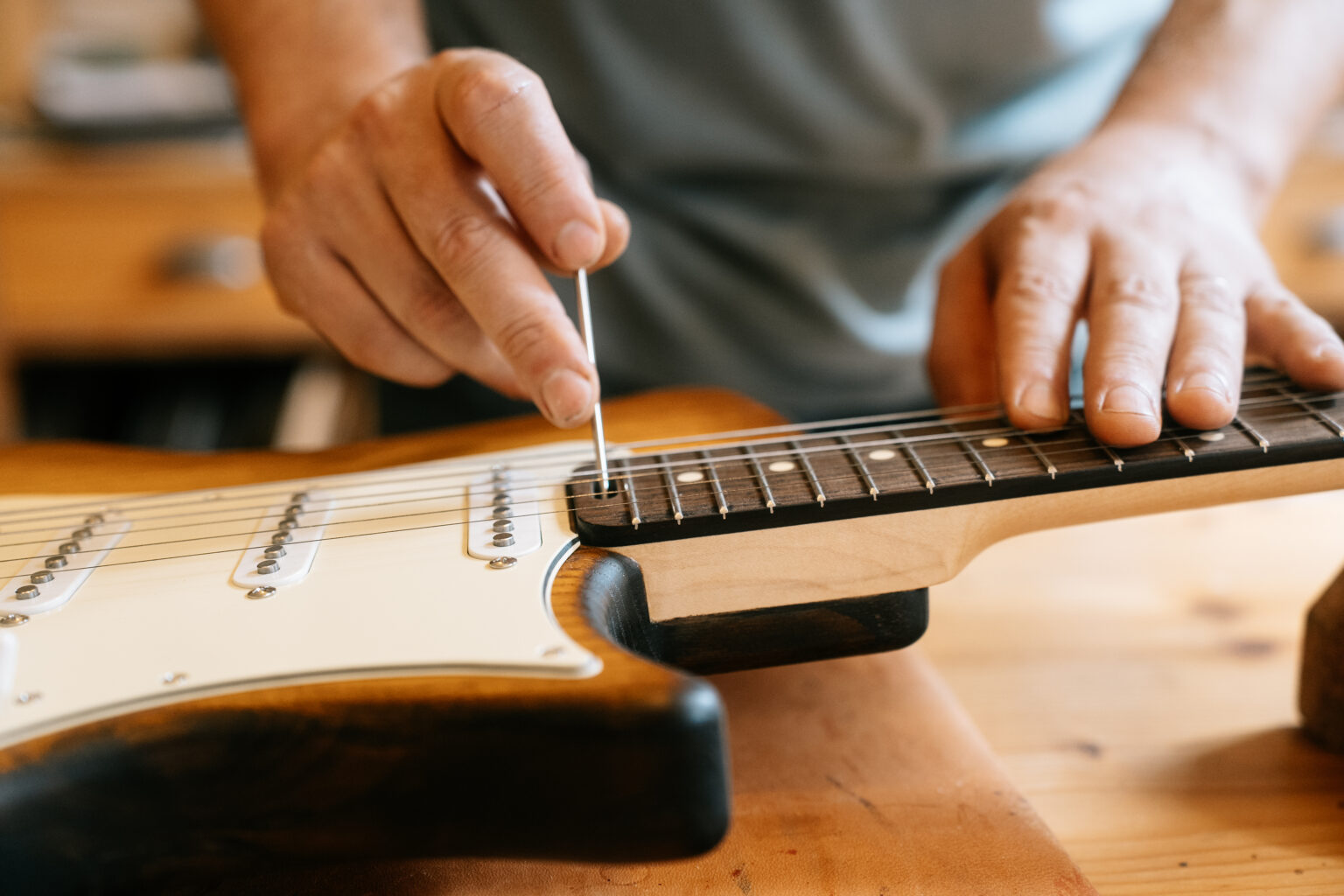 un luthier réglant le manche d'une guitare dans son atelier